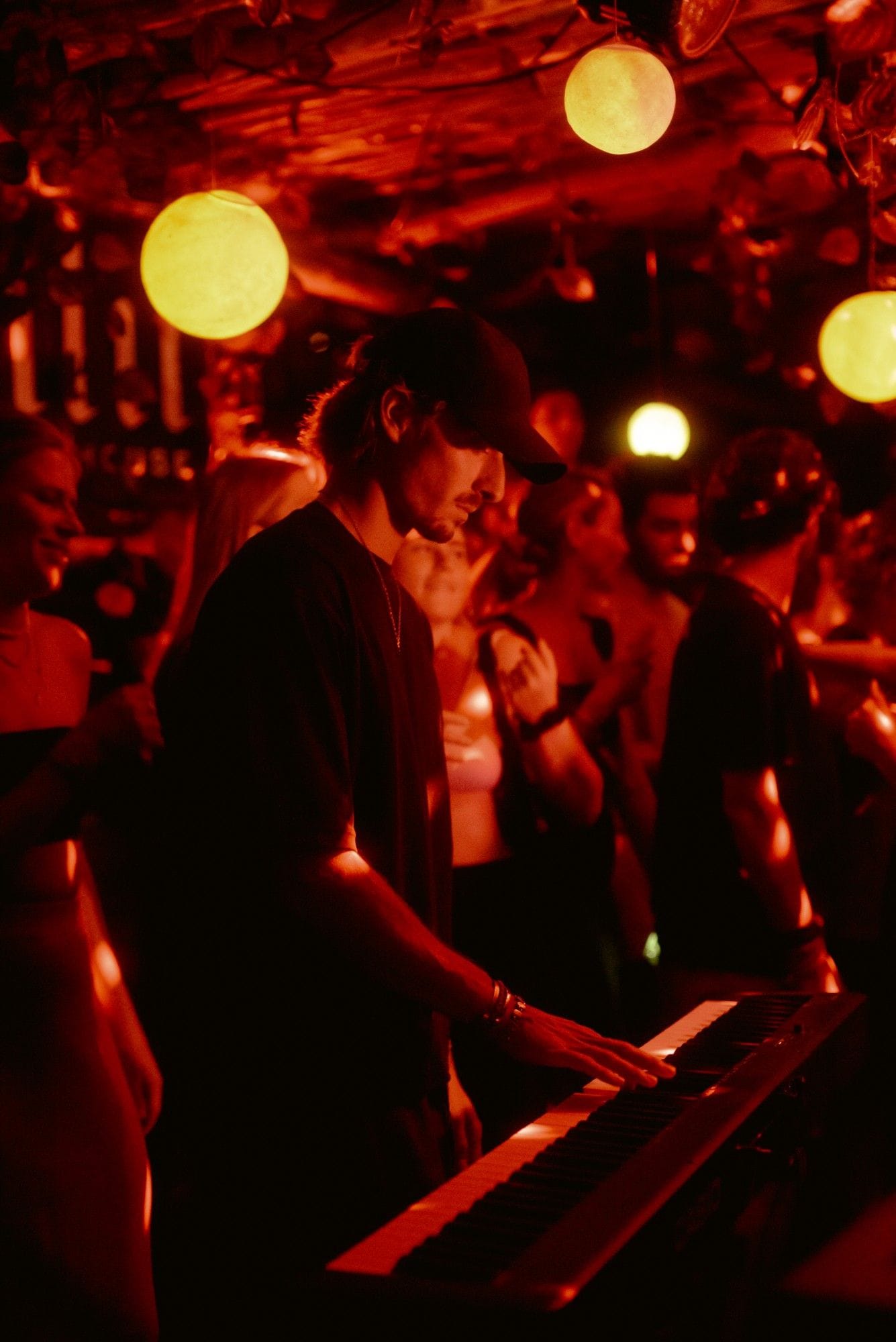 Pianofrenchy playing a keyboard in a crowded, red-lit bar at night