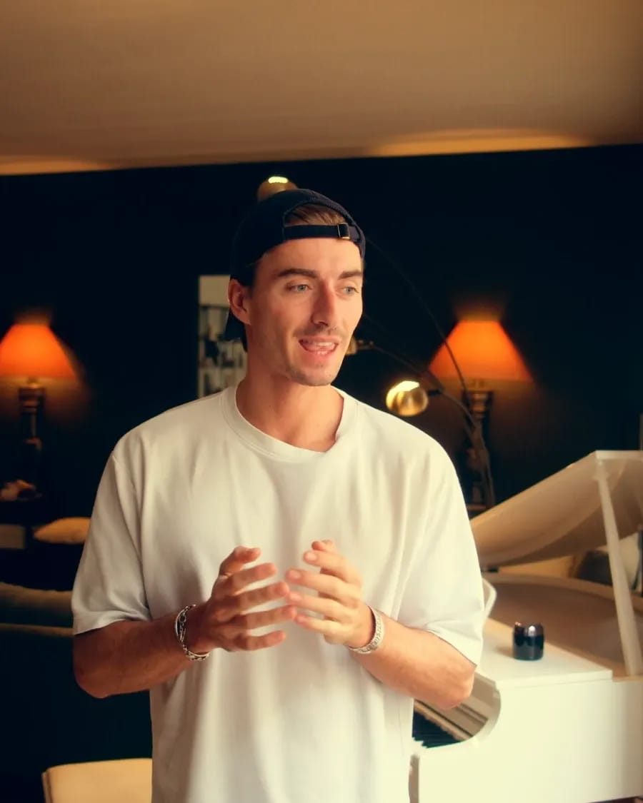 Pianofrenchy talking in a warmly lit apartment, a white grand piano behind him