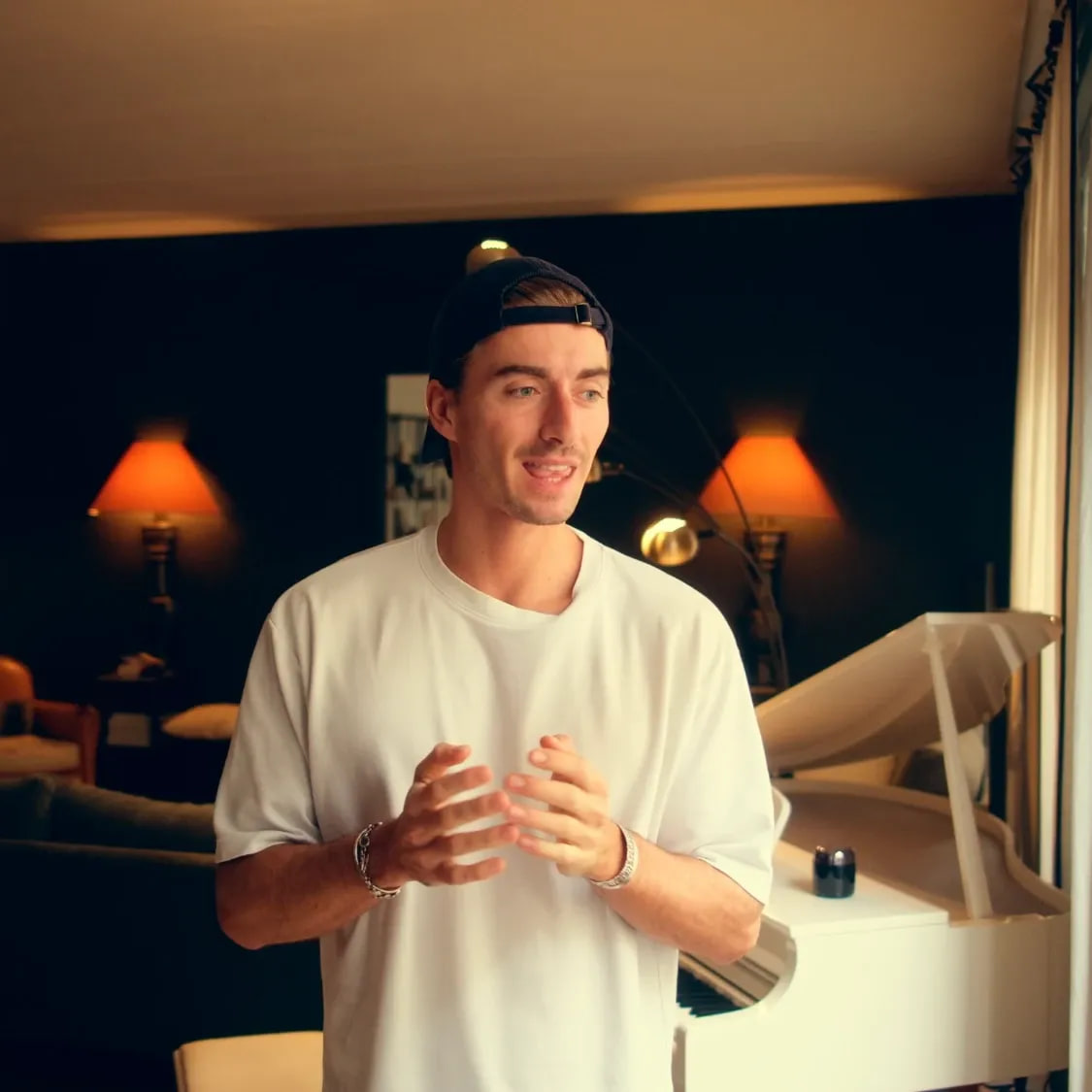 Pianofrenchy talking in a warmly lit apartment, a white grand piano behind him